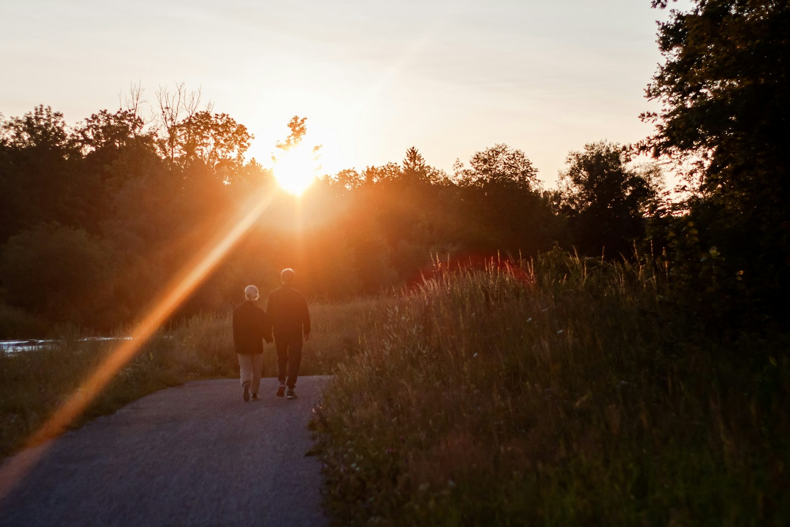 A couple walking hand in hand along a path towards the setting sun