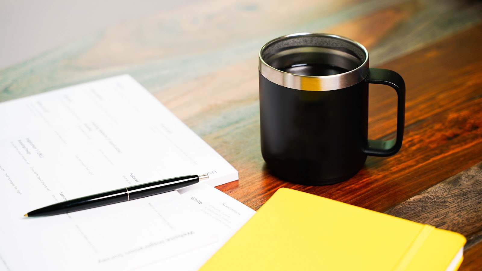 A notebook, pen and mug of coffee on a wooden desk